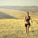 Woman running on a open hill in activewear on a hot summer day